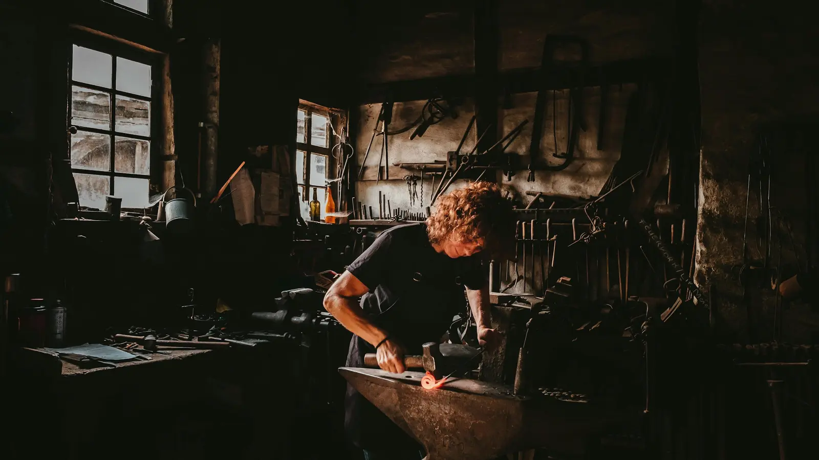 A metalworker shaping steel on an anvil in a workshop